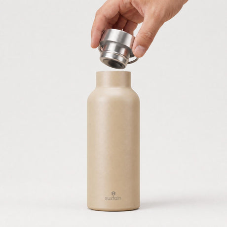 Suztain termoflaske 500 ml beige i rustfritt stål, med en hånd som holder lokket over flasken
