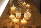 Steinhart telys stjerne 4-pakning gul i bivoks, fire tente telys og to bivokslys i glass på et trebord