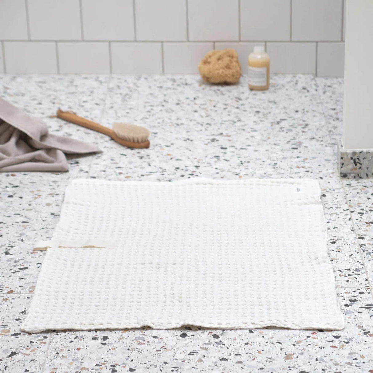 The Organic Company Big Waffle Badematte Naturlig Hvit i bomull, med badebørste og såpe i bakgrunnen