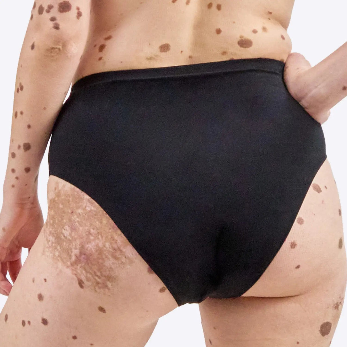 Wuka Stretch Cotton Midi Brief Heavy Flow i svart bomull, sett bakfra på en kvinnekropp med hånden i siden
