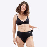 Wuka Stretch Cotton Midi Brief Heavy Flow i svart bomull, en kvinne strekker ut trusen med WUKA-logoen synlig