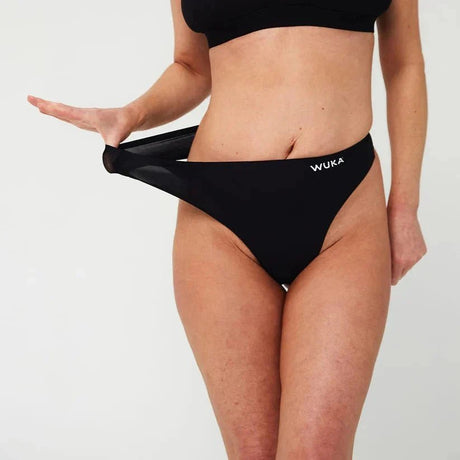 WUKA Stretch Thong Light/Medium flow svart i tekstil, modell strekker ut trusestrikken for å vise elastisitet