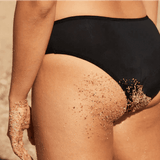 WUKA Swim Bikini Brief Light Flow Svart i stoff, i bruk på en person med sand på hud og truse